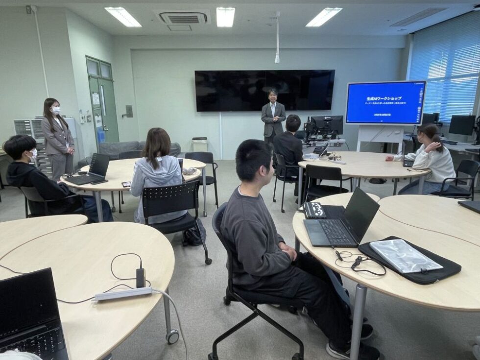 講師がスライドを用いてAIの基礎について説明しており、学生たちが前方にあるモニターの方向を向いて講義を受けている。