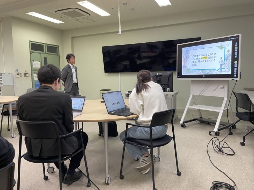 学生が、AIで生成した自分史の動画や音楽作品を発表し、前方のモニターに作品が表示され、他の学生が発表を聞いている。