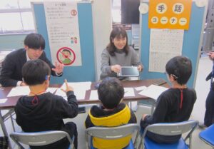 手話体験ブースの様子。児童3名が小林・田中と一緒に手話をしている